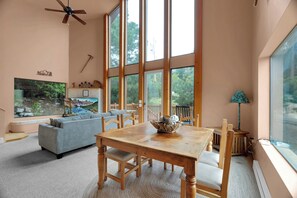 A spacious living room with a large wooden dining table, a sofa, and a large window with a view of trees.