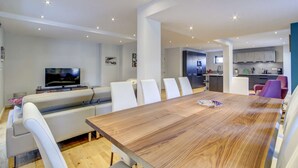 A modern living room with a wooden dining table, white sofas, and a kitchen in the background. - Very spacious apt with ground level easy access in Morzine center (MORZINE)