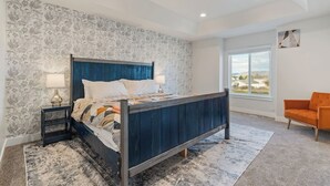 Une chambre à coucher avec un lit, des tables de chevet, un tapis, une fenêtre et un fauteuil orange.