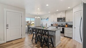 Une cuisine moderne avec des meubles blancs, un îlot central doté de tabourets, un micro-ondes encastré et une grande fenêtre offrant une vue sur l’extérieur.