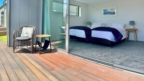 Ein modernes Zimmer mit zwei Betten, einer Glastür zum Balkon und einem kleinen Tisch mit Stuhl.