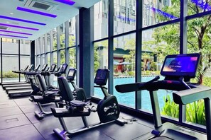 A gym with exercise equipment and a large window overlooking a pool. - Star Residence KLCC By Starlight (Kuala Lumpur)