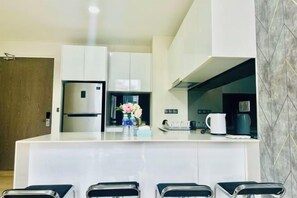 A modern kitchen with white cabinetry, a central island, and bar stools. - Star Residence KLCC By Starlight (Kuala Lumpur)