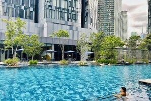 Una piscina con una persona nadando, rodeada de árboles y edificios modernos.