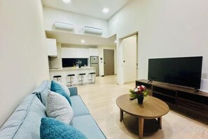 A modern living room with a sofa, a coffee table, and a TV. There is a kitchen area in the background with a bar and a large screen. - Star Residence KLCC By Starlight (Kuala Lumpur)