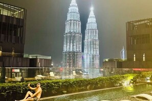 A nighttime view of the Petronas Twin Towers with a person sitting on a balcony overlooking a pool. - Star Residence KLCC By Starlight (Kuala Lumpur)