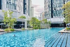 A swimming pool surrounded by modern buildings with glass facades, trees, and outdoor seating areas. - Star Residence KLCC By Starlight (Kuala Lumpur)