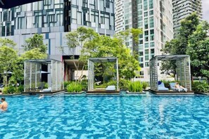 A swimming pool with lounge areas, surrounded by greenery and modern buildings. - Star Residence KLCC By Starlight (Kuala Lumpur)