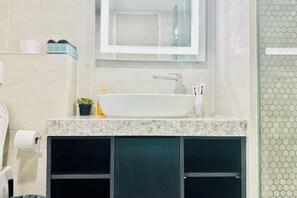 A bathroom with a white sink, a mirror above it, and a towel rack. There is a toilet paper roll on the wall and a small plant on the counter. - Star Residence KLCC By Starlight (Kuala Lumpur)
