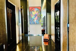 A hotel corridor with a polished floor, a colorful abstract painting on the wall, and a luggage trolley. - Star Residence KLCC By Starlight (Kuala Lumpur)
