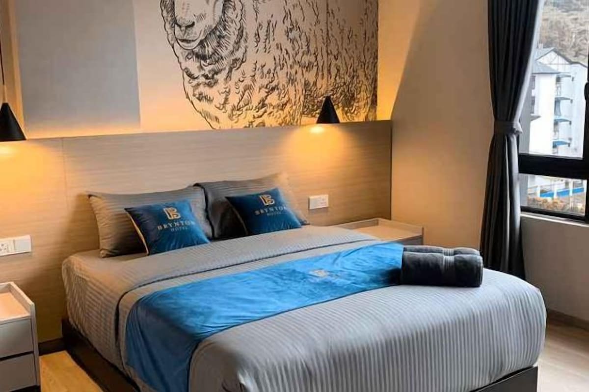 A hotel room with a bed, bedside tables, a nightstand, and a window with curtains.