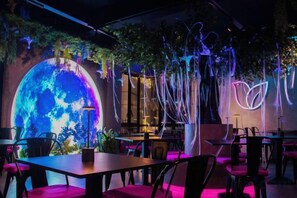 Un espace de restauration intérieur avec des tables et des chaises, un grand globe illuminé et des plantes suspendues.