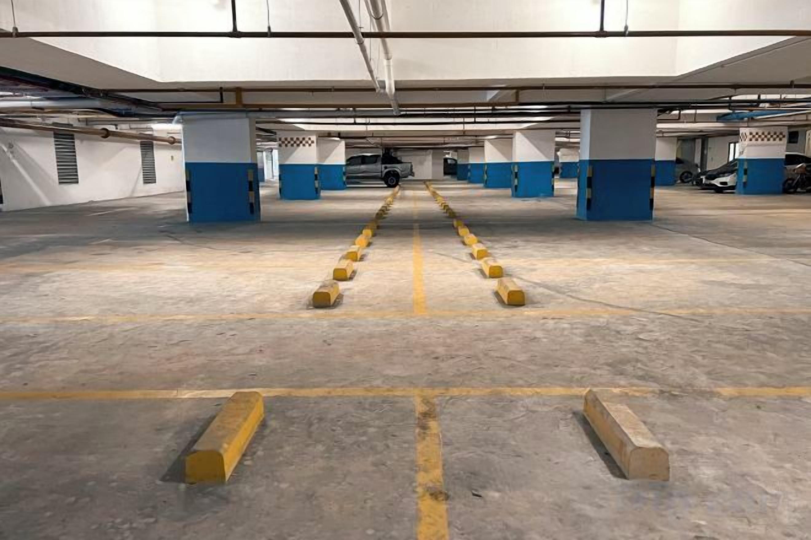 An underground parking garage with concrete floors, yellow bollards, and blue pillars.