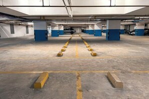 An underground parking garage with concrete floors, yellow bollards, and blue pillars. - Hotel Brynton at Cameron Centrum Mall (Brinchang)