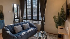 A living room with a sofa, a glass coffee table, a large window with curtains, and a potted plant. - Hotel Brynton at Cameron Centrum Mall (Brinchang)