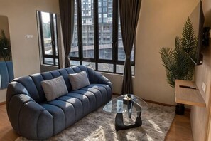 A living room with a sofa, a glass coffee table, a large window with curtains, and a potted plant. - Hotel Brynton at Cameron Centrum Mall (Brinchang)