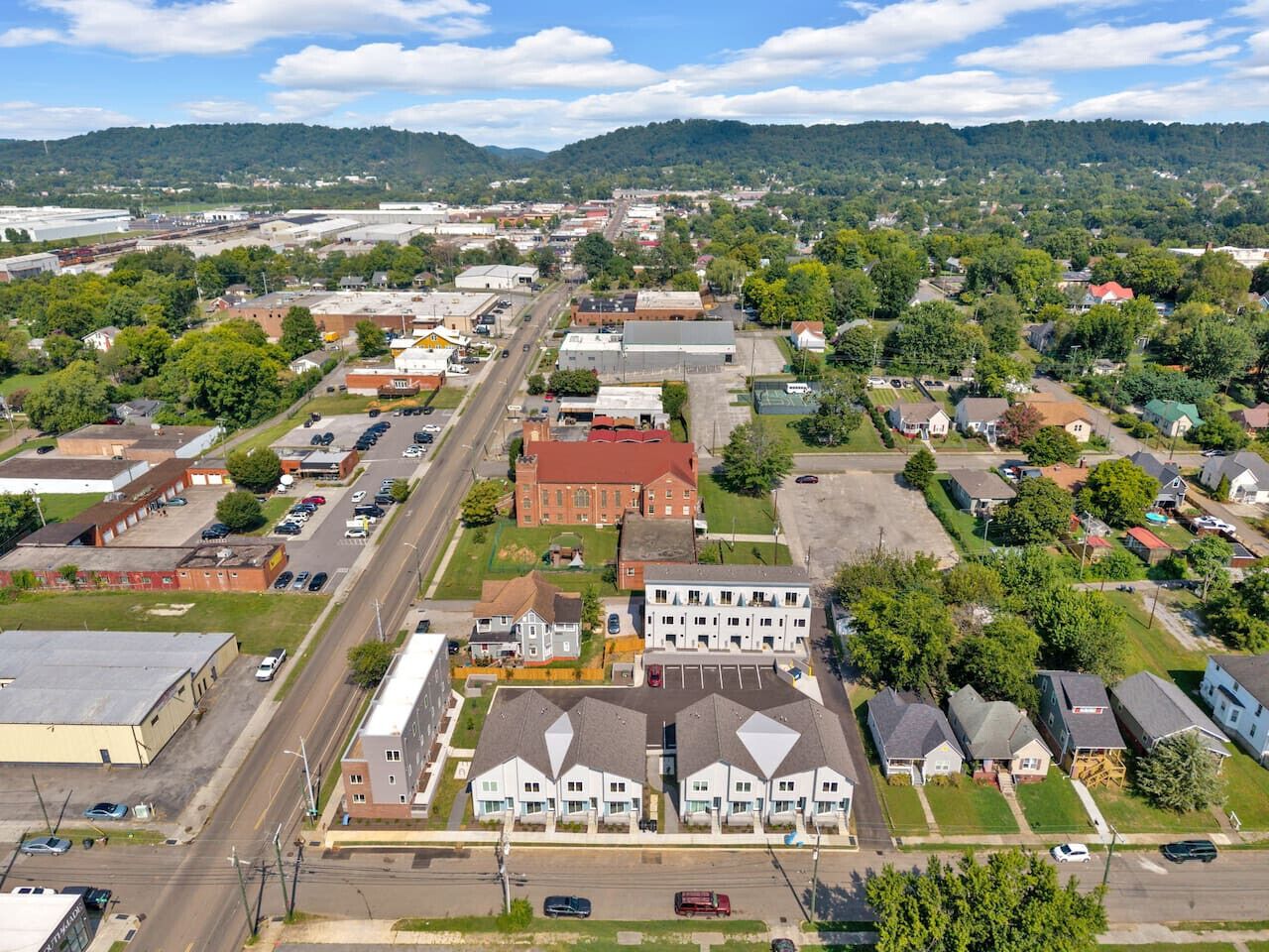 An aerial view of a town with a mix of residential and commercial buildings, including a prominent red brick building and several white apartment complexes.