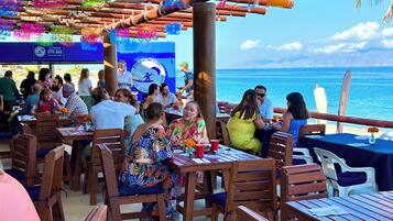 Un restaurant situé en bord de mer, avec des tables et des chaises en bois, une vue sur l’océan et une enseigne indiquant « Paradis du kitesurf ».