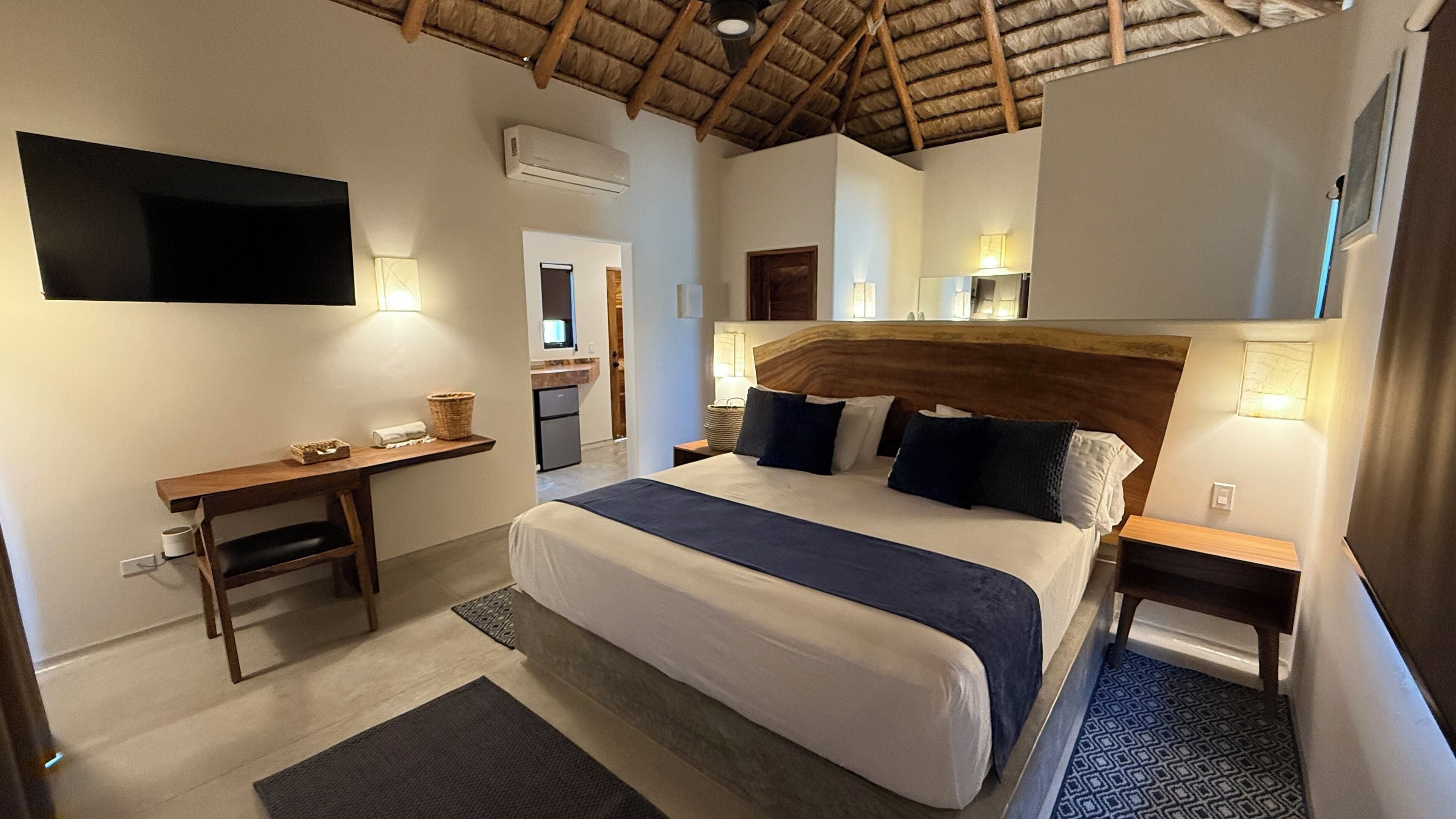 A hotel room with a bed, a desk, a TV, and a kitchenette.