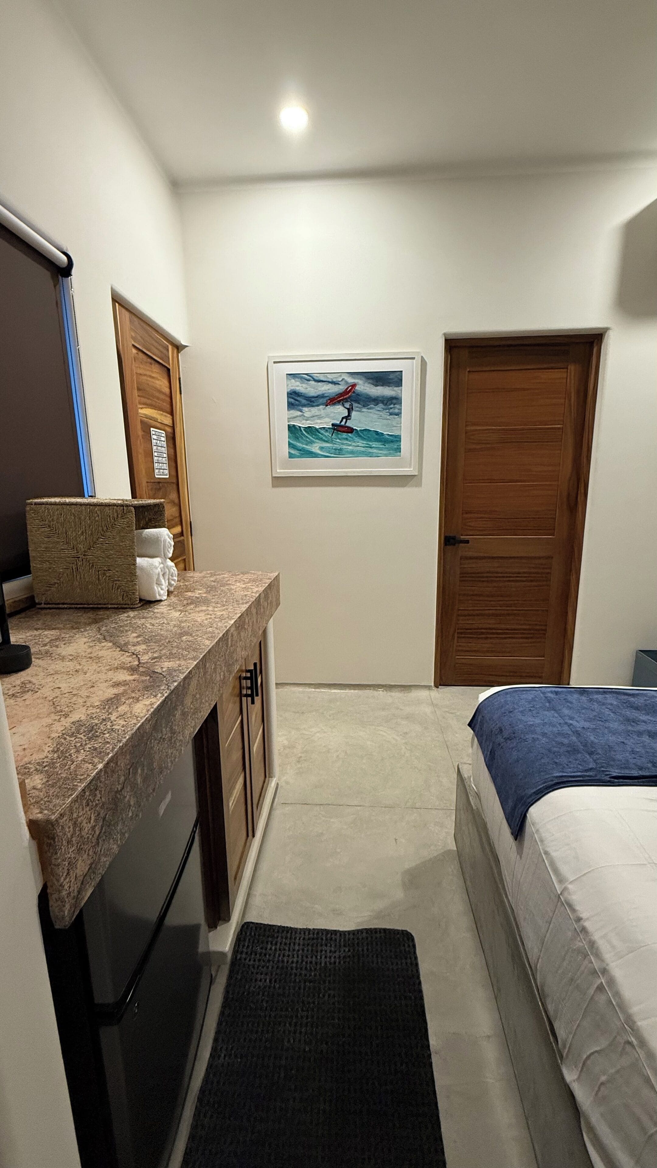 A hotel room with a bed, a desk with a computer, a sink, and a framed picture on the wall.