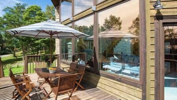 Een houten terras met een glazen patio, tuinmeubilair en uitzicht op een zwembad.