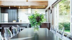 Een moderne keuken met een eethoek, met een groot raam, houten balken in het plafond en een centrale tafel met stoelen.