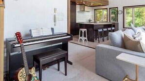 Een woonkamer met een piano, een gitaar, een bank en een keukenbar.