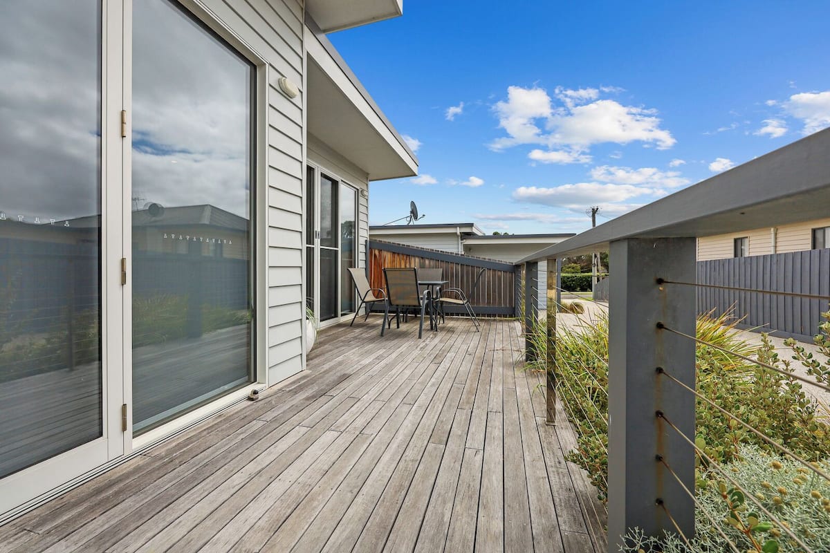 A wooden deck with a sliding glass door leading to a patio area with a table and chairs.