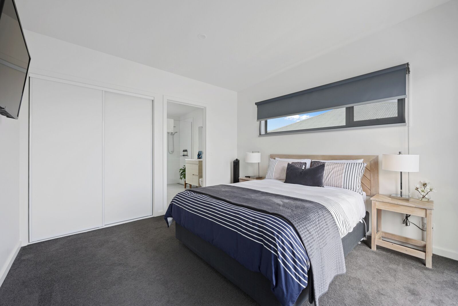 A modern bedroom with a large bed, a bedside table with a lamp, a wardrobe, and a window with a view.