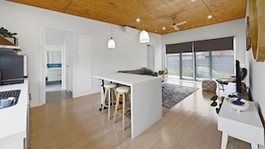 Een moderne keuken met een centraal eiland, een paar barkrukken, hanglampen en een groot raam met uitzicht op de omgeving.