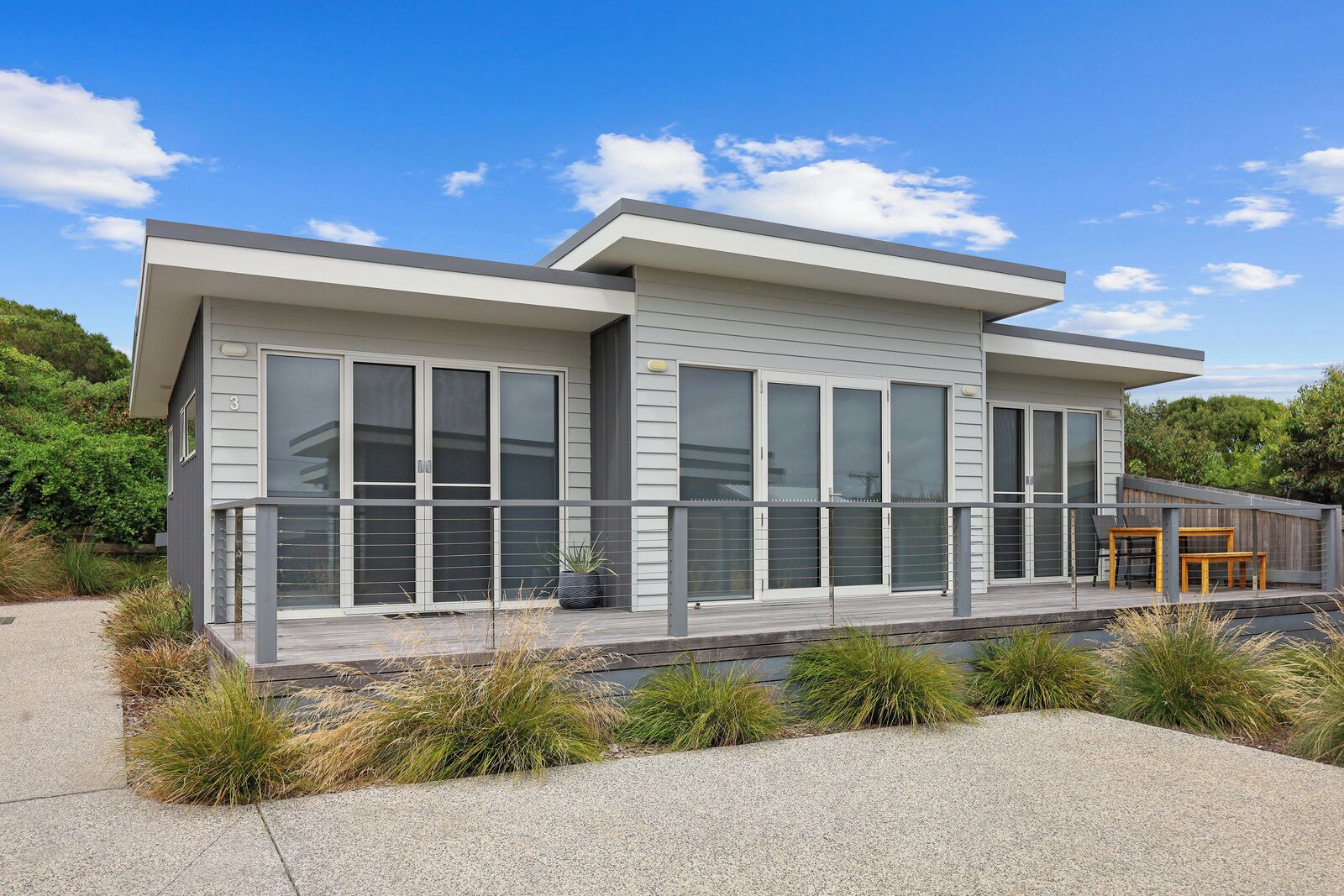 A modern two-story house with large windows, a covered porch, and outdoor seating.