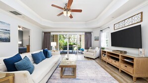 Un salon doté d’un ventilateur de plafond, d’un canapé avec des coussins bleus, d’une table basse, d’un téléviseur et d’un meuble de rangement en bois pour les appareils multimédias.