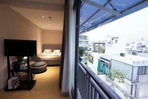Een moderne kamer met een bed, een tv op een standaard, een klein tafeltje en uitzicht op gebouwen.