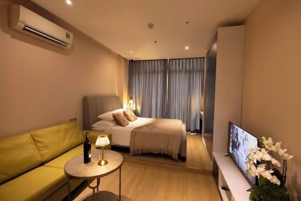 Een hotelkamer met een bed, een bank, een televisie en een kleintje tafeltje met een fles en een lamp.