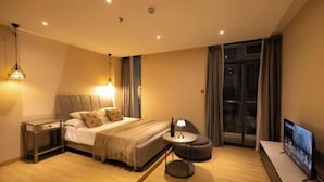 Een moderne hotelkamer met een groot bed, nachtkastjes, een televisie en uitzicht op de stad 's nachts.