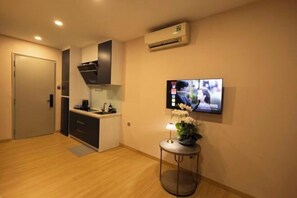 Een moderne keuken met een ingebouwde oven, een magnetron en een koffiezetapparaat. Er is een flatscreen televisie aan de muur bevestigd, en een kleine tafel met een potplant.