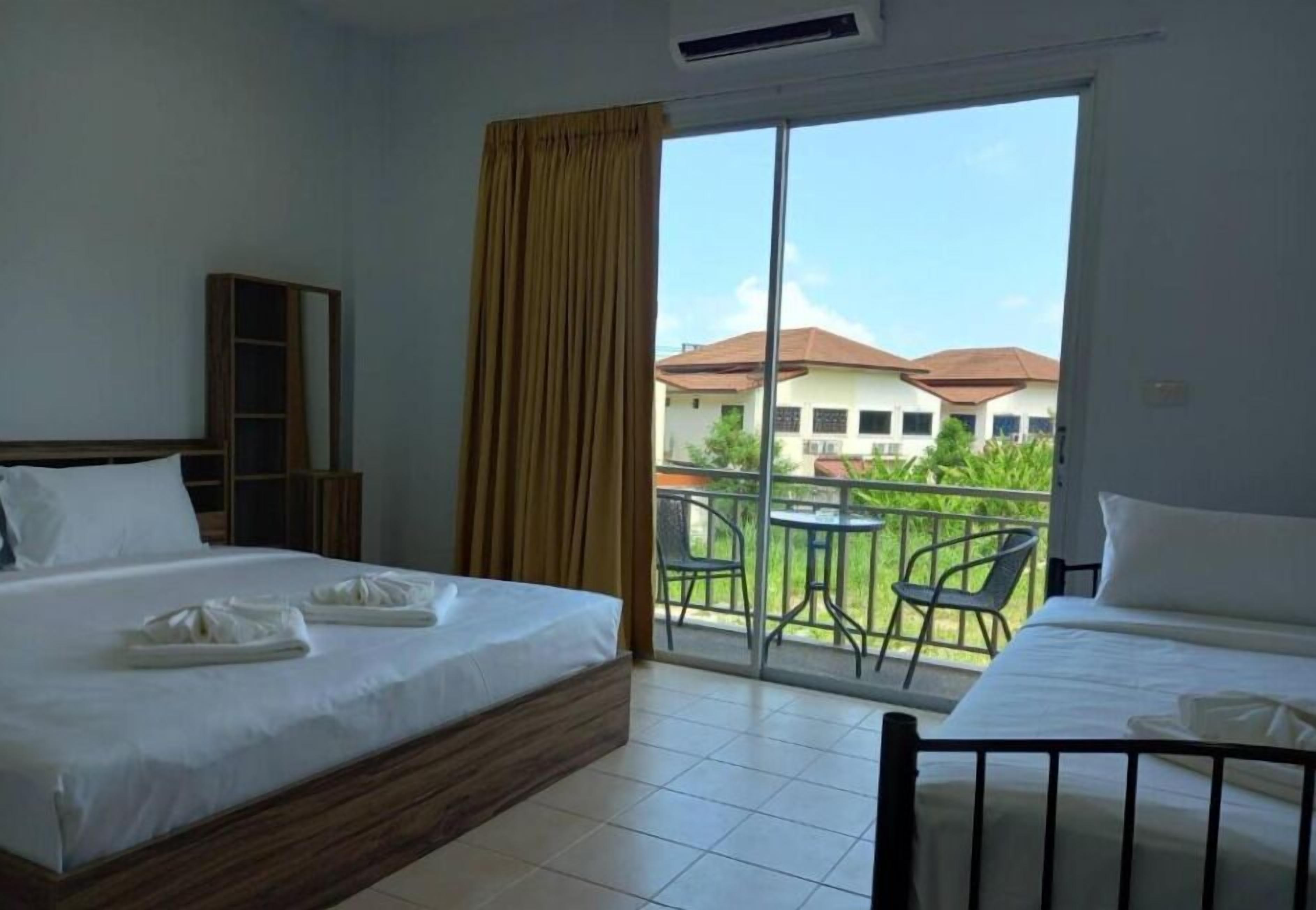 Habitación de hotel con dos camas, puerta corrediza al balcón y vista a edificios en la distancia.