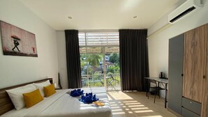 A hotel room with a bed, a desk, a wardrobe, and a balcony with a view of palm trees. - L&P Guesthouse (Karon)