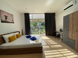 Habitación de hotel con cama, escritorio, armario y balcón con vistas a palmeras.