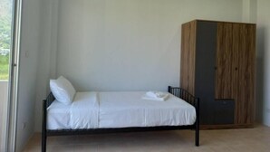 A single bed with white bedding in a room with a wooden wardrobe and a window. - L&P Guesthouse (Karon)