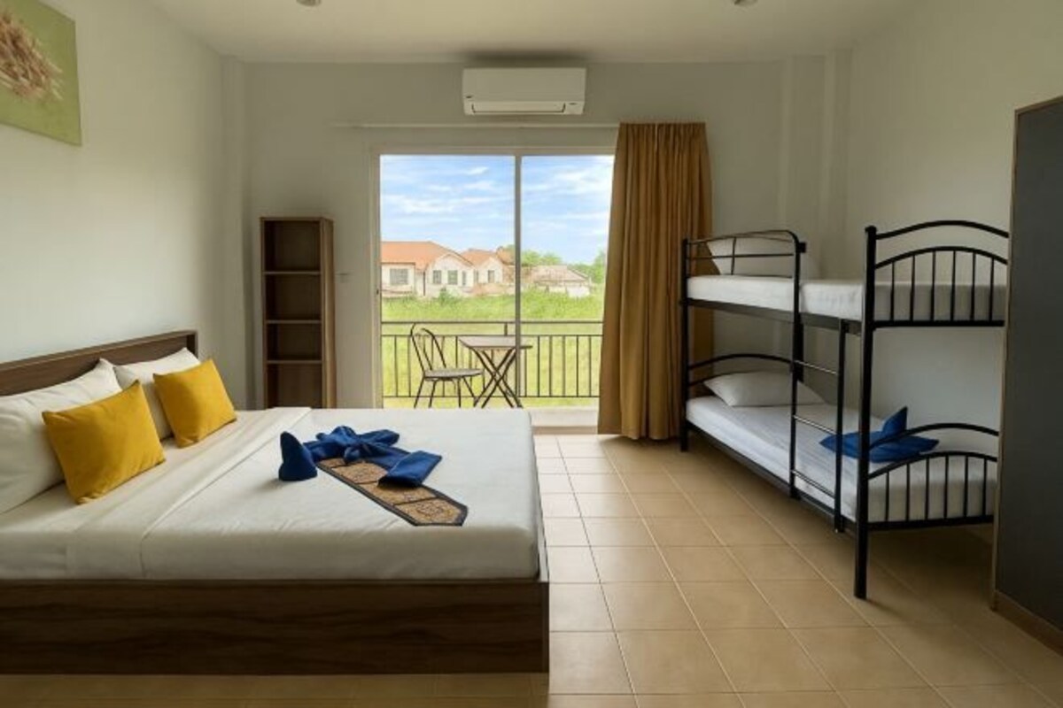 A hotel room with a bed, bunk beds, a balcony with a table and chairs, and a view of buildings.