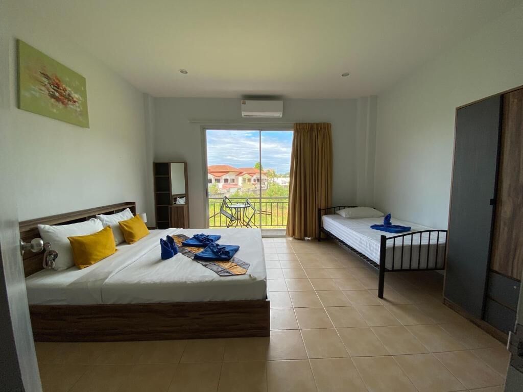 A hotel room with a bed, a desk, a chair, and a balcony with a view of buildings.
