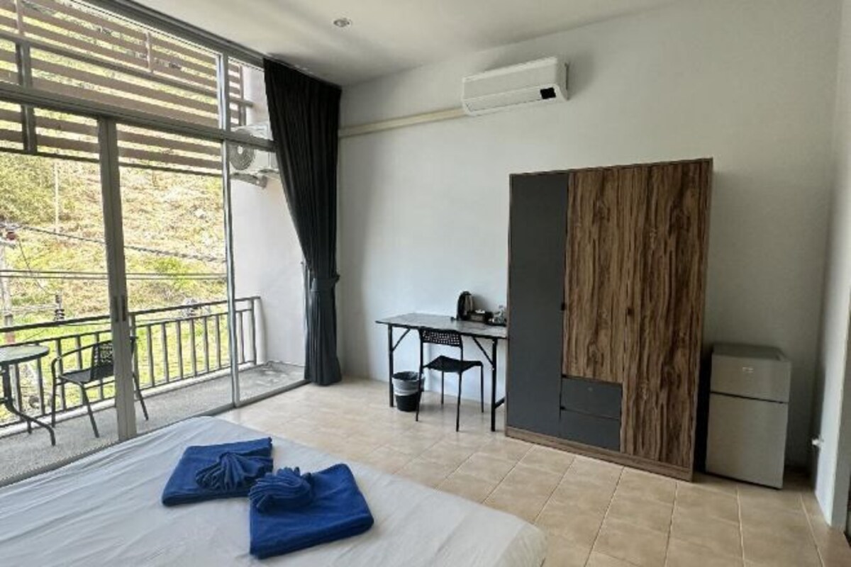 A hotel room with a bed, a desk, a small table, a balcony, and a wardrobe.