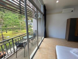 Habitación de hotel con balcón, una cama, una mesa con sillas y vistas a zonas verdes y edificios.
