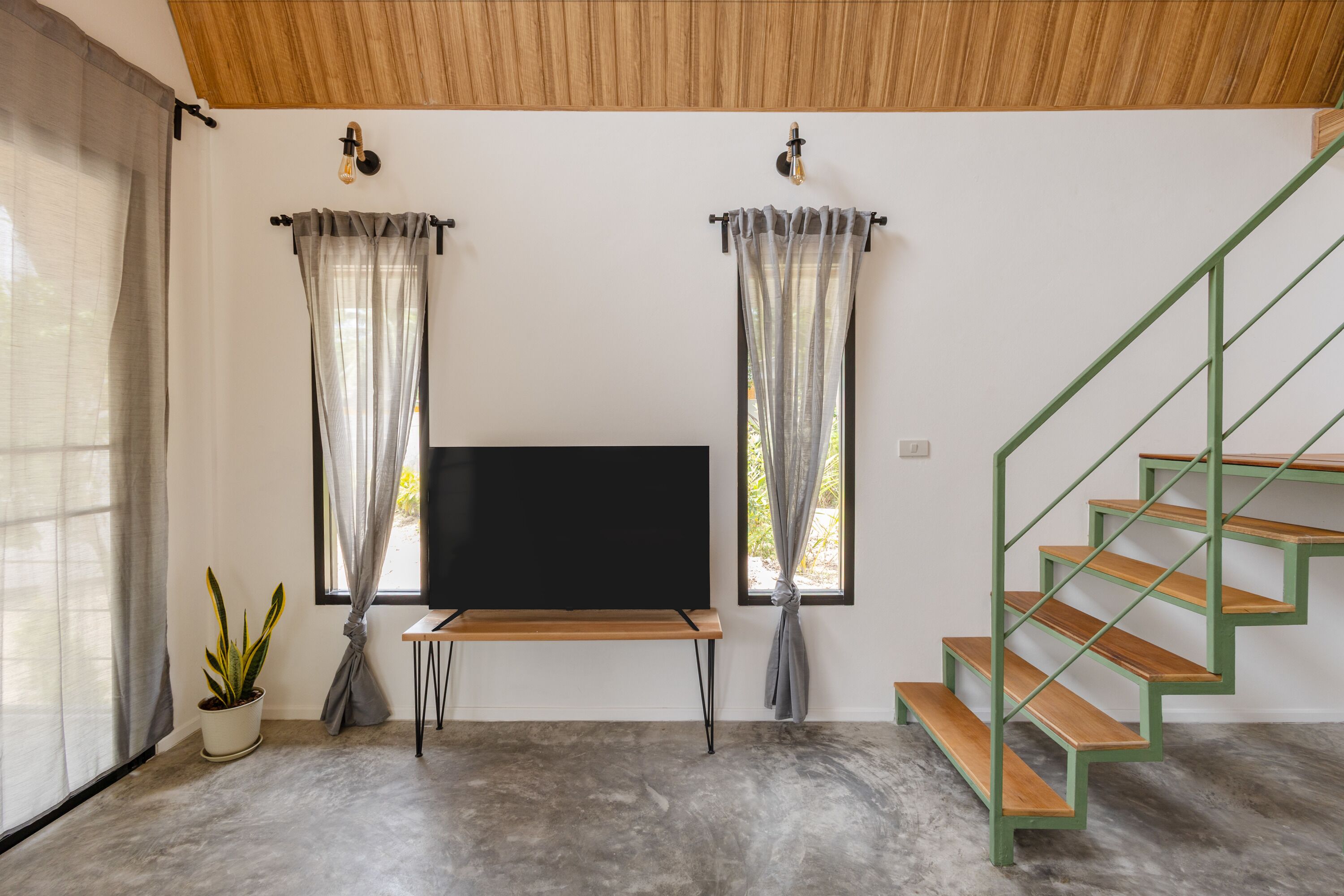 A room with a wooden bench, a TV, a staircase, and a potted plant.