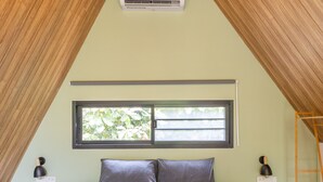 A bedroom with a sloped ceiling, a bed, a window, and an air conditioning unit. - Coconut WayWay Retreat by Sea N' Rent (Ko Pha-ngan)