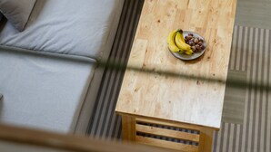 A modern living room with a grey sectional sofa, a wooden coffee table with fruits, and a glass door leading to an outdoor area. - Coconut WayWay Retreat by Sea N' Rent (Ko Pha-ngan)