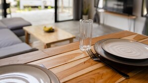 A dining area with a wooden table set for two, a glass of water, and a television in the background. - Coconut WayWay Retreat by Sea N' Rent (Ko Pha-ngan)