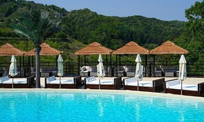 A swimming pool with lounge chairs and thatched umbrellas, surrounded by lush greenery. - Chuncheon bali 376 (Chuncheon)