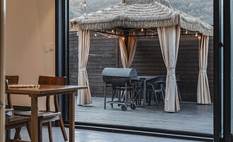 An outdoor dining area with a wooden deck, a grill, and a thatched gazebo.